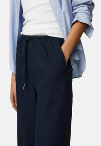 Marineblauwe linnen broeken met een elastische tailleband en trekkoord. Zijkantenzakken en een ontspannen pasvorm, gecombineerd met een lichtblauw overhemd met knopen.