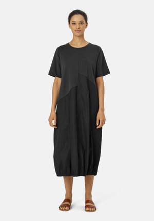 Black dress made of cotton blend with short sleeves, asymmetric design, and elastic hem. Paired with brown sandals for a casual look.