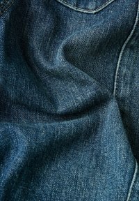Denim fabric in a dark blue hue, featuring twill weave texture and slight sheen. Includes visible stitching along the edges and pockets.