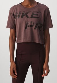Maroon cropped Nike t-paita, jossa on rohkea musta "NIKE" ja "PRO" -teksti. Lyhythihaiset, pehmeä kangas ja rento istuvuus. Yhdistetty tummiin leggingeihin.