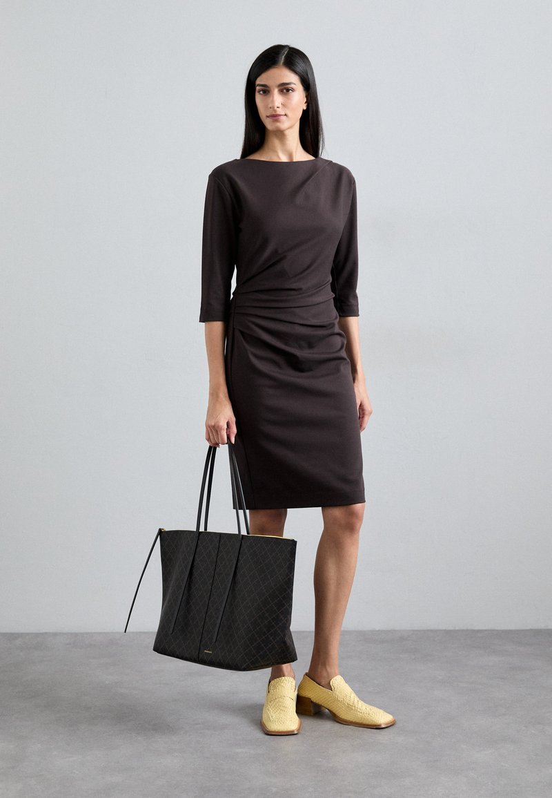 Abito marrone fitted con maniche a tre quarti, dettaglio arricciato in vita, abbinato a una borsa a tracolla nera texture e scarpe gialle intrecciate.