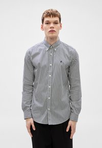 Πουκάμισο με κουμπιά σε ρίγες σε ναυτικό μπλε και λευκό, με γιακά, μακριά μανίκια και μικρό λογότυπο στο στήθος. Λείο ύφασμα.