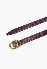 Fioletowy skórzany pasek z teksturowanym wzorem przypominającym skórę węża. Złota owalna klamra zdobiona jest szczegółowym wzorem liścia oraz błyszczącymi akcentami.