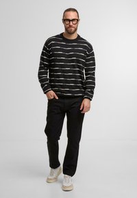 Maglione a strisce nere con linee orizzontali bianche, abbinato a pantaloni neri e sneaker con dettagli beige, caratterizzato da una vestibilità rilassata.