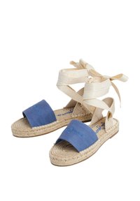 Sinine kangast espadrillid, millel on punutud jute tallad ja beežid ribad logotähtede detailiga, mõeldud ankru sidumiseks.