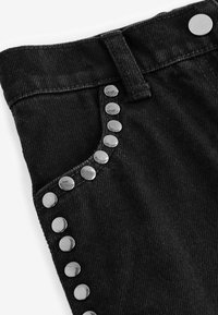 Svart denim med en slät textur som har en rad av glänsande metallknappar längs fickkanten och en knappstängning i midjan.
