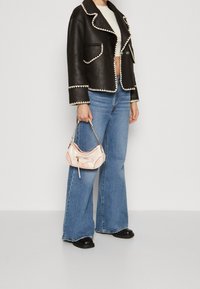 Veste en cuir noir avec coutures blanches, coupe courte. Jean bleu clair évasé. Petit sac rose avec bandoulière en chaîne et détail zippé.