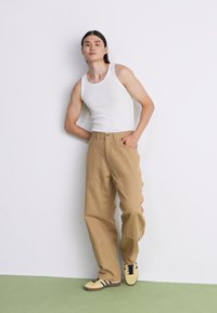 White tank top, tan wide-leg pants, and beige sneakers with black stripes. Simple design and smooth texture against a neutral background.