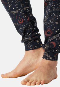 Laivansiniset legginsit, joissa on taivaallinen kuvio kultaisista tähdistä ja punaisista yksityiskohdista. Yksityiskohtia ovat tiukka nilkkahihna ja yksinkertaiset varpaat.