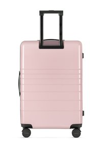 Rosa Hartschalenkoffer mit horizontalen Rillen, ausziehbarem schwarzen Griff und vier schwarzen Rädern für Mobilität. Stilvolles und kompaktes Design.
