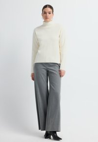 Biała sweter turtleneck zestawiona z szarymi spodniami typu wide-leg. Stworzoną stylizację uzupełniają czarne botki na obcasie z ostrym noskiem. Prosty design i faktury.