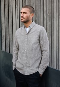 Camisa de botones de manga larga con un patrón geométrico en blanco y negro, que presenta un cuello y un corte relajado, combinada con pantalones oscuros.