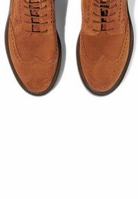 Scarpe brogue in suede marrone con chiusura a lacci, dotate di perforazioni decorative e dettagli a punta nelle parti anteriore e laterale.