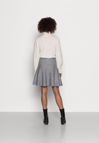 Falda acampanada gris claro combinada con un suéter crema, que presenta un cuello alto y mangas abullonadas. Botines negros completan el conjunto.