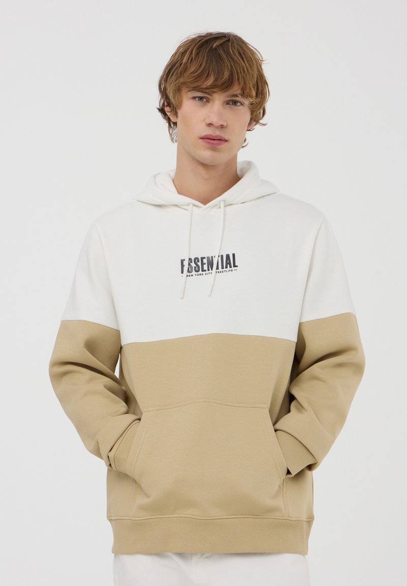 Felpa con cappuccio caratterizzata da una parte superiore bianca e una parte inferiore beige. Include una tasca frontale e un logo stampato. Tessuto morbido.