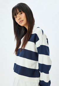Maglione a righe blu navy e bianco con colletto, caratterizzato da una vestibilità comoda e maniche lunghe. Tessuto morbido e texture visibile nel materiale.