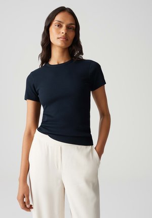 T-shirt fitted color blu navy con maniche corte e scollatura rotonda, realizzato in tessuto a costine; abbinato a pantaloni larghi color crema.