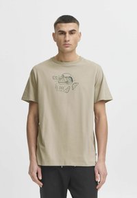 Beige cotton t-shirt featuring a black graphic print of fish and text "EL ORO DEL MAR" on the front, with a relaxed fit and short sleeves.
