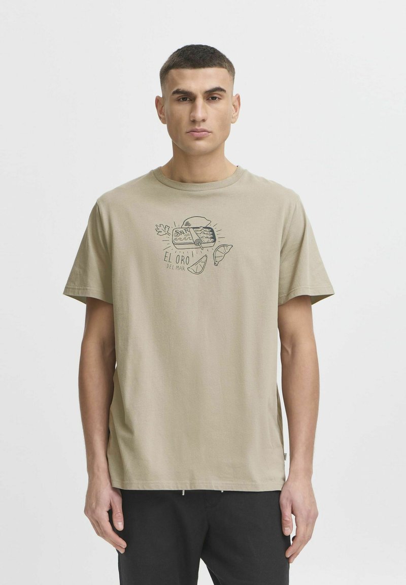Beige cotton t-shirt featuring a black graphic print of fish and text "EL ORO DEL MAR" on the front, with a relaxed fit and short sleeves.