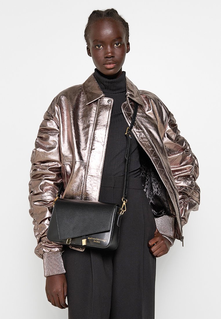 Metalowa pomarańczowa kurtka puchowa z prążkowanymi mankietami, czarny golf i czarna skórzana torebka na ramię z złotym zapięciem i logo.