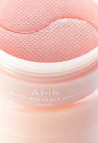 Pot pour patch oculaire rétinien PDRN avec une surface en gelée rose texturée. Le couvercle transparent révèle la consistance du gel, étiqueté avec le nom de la marque et les détails du produit.