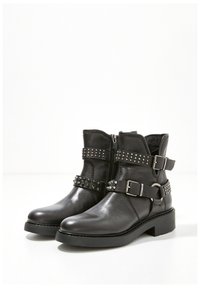 Black ankle boots made of leather with studded straps, buckles, and a side zipper. The sole is flat with a modest heel.