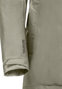Manche de veste verte résistante à l'eau avec une finition texturée, dotée d'une sangle Velcro et du logo "Texapore" en gris foncé sur le poignet.