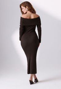 Geripptes, schulterfreies dunkelbraunes Kleid mit langen Ärmeln und enger Silhouette. Glatte Textur und midilanger Schnitt.