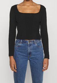 Crop top noir à manches longues côtelé avec un col carré, associé à un jean bleu taille haute avec un design classique à cinq poches.
