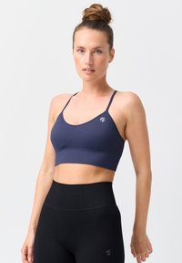 Marineblauer, gerippter Sport-BH mit dünnen Trägern und einem Logo-Detail, kombiniert mit hochgeschnittenen, schwarzen, gerippten Leggings. Glatte Textur und taillierte Passform.