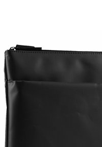 Funda negra con cremallera hecha de un material texturizado. Presenta una parte superior suave, con un bolsillo frontal que tiene detalles de costura sutiles.