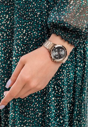 Montre-bracelet dorée avec un cadran gris rond, trois sous-cadrans et un bracelet en maillons. L'écran présente un indicateur de date et un accent rouge.