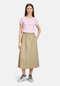 Lichtroze t-shirt met de tekst "SERIOUSLY?", gecombineerd met een khaki middellange rok en zwart, witte en paarse sneakers. De rok heeft zijzakken.