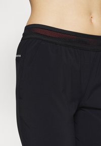 Pantalones cortos deportivos negros con una cintura de malla texturizada roja y bolsillos laterales, fabricados con un tejido ligero y elástico.