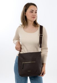Braune Leder-Schultertasche mit strukturierter Oberfläche, mit einer vorderen Reißverschlusstasche und einem gemusterten, verstellbaren Schulterriemen.