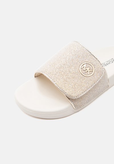 Λευκό σανδάλι με εύκαμπτο, λαμπερό λουράκι με κυκλικό μεταλλικό λογότυπο MK στο πλάι.