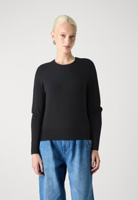 Maglione nero a maglia con maniche lunghe e scollo rotondo, abbinato a un paio di jeans in denim larghi. Texture liscia, vestibilità comoda.