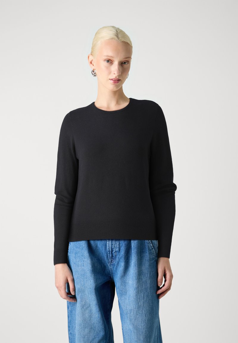 Maglione nero a maglia con maniche lunghe e scollo rotondo, abbinato a un paio di jeans in denim larghi. Texture liscia, vestibilità comoda.