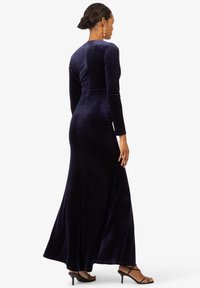 Navyblaues Samt-Maxikleid mit langen Ärmeln und tailliertem Oberteil, das mit einem dezenten Rüschendetail an der Taille und einem ausgestellten Saum versehen ist.