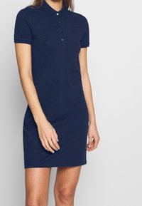 Vestito polo blu navy in cotone, dotato di colletto, maniche corte e apertura con bottoni. Logo sottile sul petto.