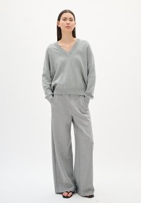 Pull en V ample gris à manches longues associé à un pantalon large gris. Texture douce, design minimaliste et sans motifs visibles.