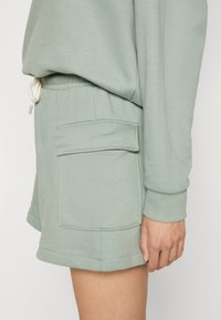 Shorts vert menthe en tissu doux, avec une taille élastique munie d'un cordon de serrage et deux poches avant à rabat.