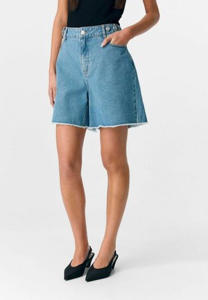 Shorts en denim bleu clair avec taille haute, deux poches avant et ourlet brut. Associés à des escarpins noirs à bout pointu.