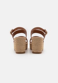 Brune lærplattform sandaler med flettede jute kilehæler. To bakremmer har et spenne-aksent. Glatt tekstur og avrundet form.