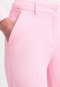 Roze textuur broek met een slim fit, zijzakken en een knoopsluiting. Heeft zichtbare stiksels en een gladde tailleband.