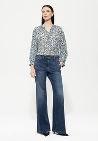 Bluse mit Blumenmuster in Hellblau mit Knopfdetails und langen Ärmeln, kombiniert mit hochtaillierten, dunkelblauen Jeans mit weitem Bein und Knöpfen.