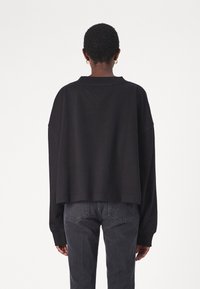Felpa nera oversize con un collo alto e spalle scese, abbinata a jeans grigio scuro. Design minimalista e texture morbida.
