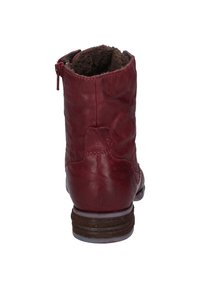 Bota de cuero rojo hasta el tobillo con un acabado texturizado, forro de pelaje sintético marrón, tacón plano y cierre de cremallera en el costado.
