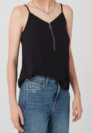 Osoba ubrana w czarny top bez rękawów z zamkiem z przodu i niebieskie jeansy z denimu, pokazana od szyi do bioder na jasnym tle.
