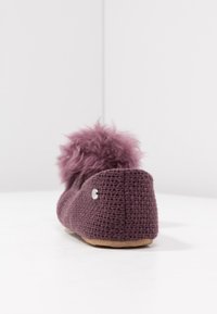Fioletowy, dziany kapcie z puszystym pomponem, płaską podeszwą i małym metalowym logo po boku. Teksturowana tkanina zewnętrzna.